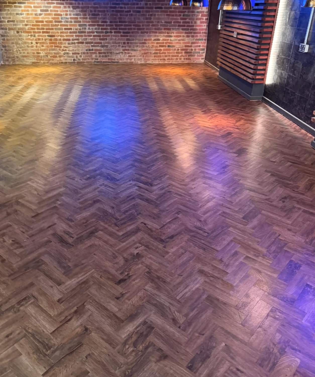 Dark herringbone flooring fitted in a commercial interior with exposed brick wall